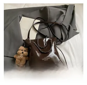 Détail sac seau marron en cuir avec poignée chaîne en métal et pendentif ours mignon