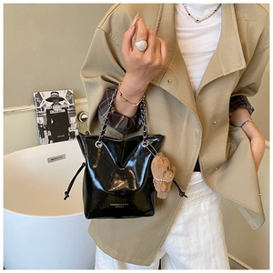 Detail of black glossy bucket bag with chain strap and teddy bear charm on beige coat