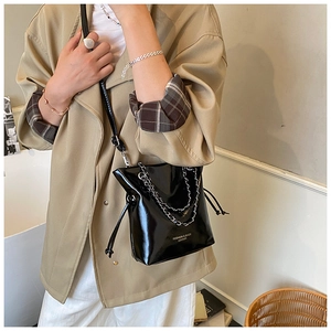 Detail of black glossy bucket bag with silver metal chain straps on a model