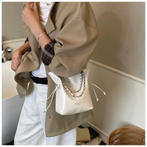 White glossy bucket bag with silver chain strap shown styled with a trench coat