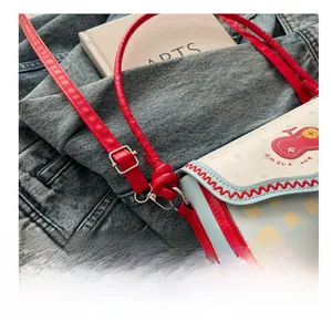Detail of checkered crossbody bag with red wavy stitching and artistic embroidery