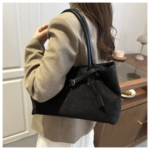 Detail of minimalist black suede tote bag with side metal buckle strap on a shoulder