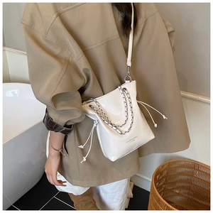 Close-up of a white patent leather bucket bag with silver chain and drawstring detail
