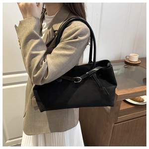 Detail of black suede tote bag with long rounded handles and stylish metallic buckle