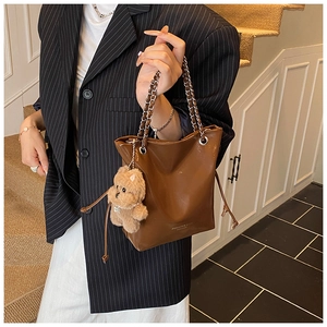 Brown bucket bag featuring a chain strap and a cute plush teddy bear charm accessory