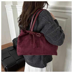 Detail view of burgundy suede tote bag with golden buckle and leather strap on model