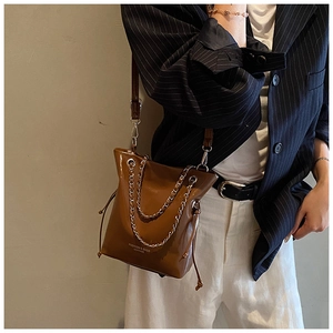 Brown glossy leather bucket bag with silver chain detail on striped blazer model