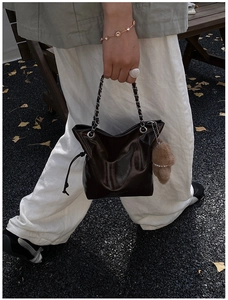 Macro view of dark brown glossy leather bucket bag featuring a silver chain and bear charm