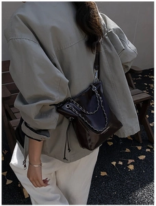 Detail of dark brown chain bucket bag with glossy finish and drawstring closure on a model