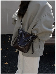 Détail du sac seau en cuir noir brillant avec double chaîne argentée et cordon de serrage