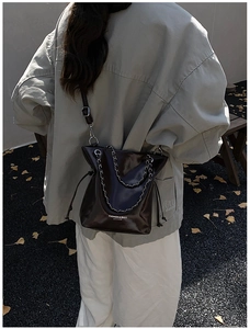 Dettaglio di una borsa a secchiello in pelle marrone scuro con catena e chiusura a cordoncino