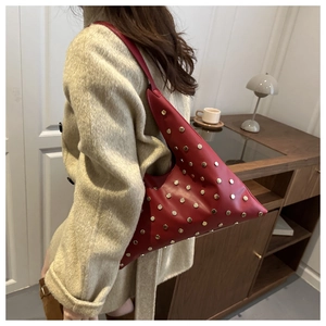 Detailed view of a red triangular leather handbag with gold studs on a beige coat