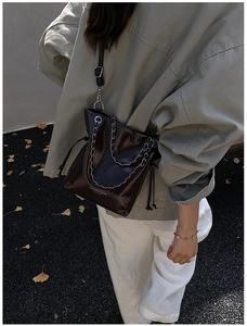 Détail d'un sac seau en cuir brillant avec chaîne argentée et fermeture à cordon