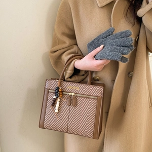 Brown leather handbag with herringbone pattern and decorative bead charm carried by model