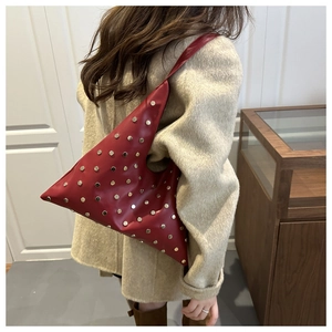 Détail du sac à épaule en cuir rouge avec rivets argentés et silhouette asymétrique chic