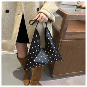 Détail du sac à bandoulière triangulaire noir avec clous métalliques dorés sur cuir mat