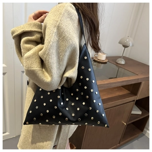 Détail du sac à bandoulière triangulaire noir avec clous dorés sur manteau beige