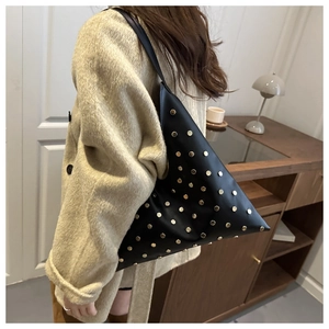 Détail d'un sac bandoulière triangulaire en cuir noir avec rivets dorés porté