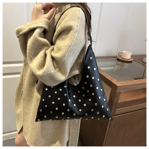 Détail d'un sac à bandoulière noir avec rivets dorés sur une finition type cuir