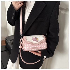 Detail of pink and white crossbody bag with apple badge and bow, worn with black blazer