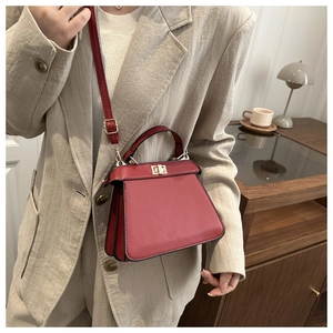 Close-up of red trapezoidal handbag featuring a gold twist lock and accordion structure