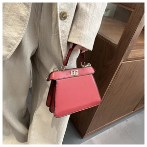 Close-up of red leather handbag with gold twist lock on beige blazer background