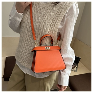 Détail d'un sac à main orange en cuir avec fermoir doré sur une tenue beige