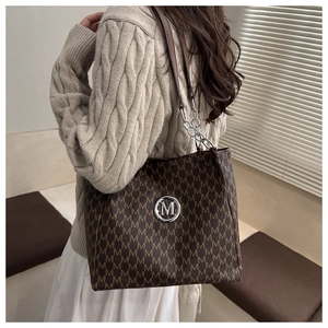 Close-up of printed tote bag featuring metallic M logo and leather chain shoulder strap
