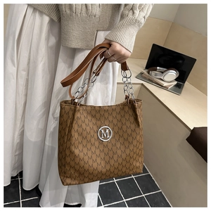 Detail der braunen Shopper-Tasche mit M-Muster, silbernem Logo und Kettenriemen