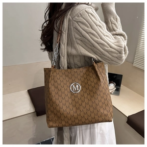 Detail of a brown tote bag featuring all-over M prints and silver chain leather strap