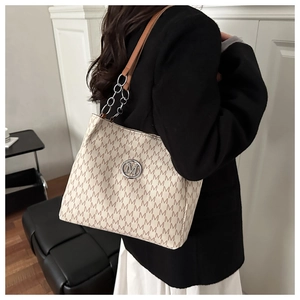 Detail of monogram tote bag with silver M logo and leather chain strap in use