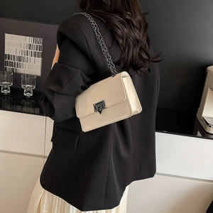 Borsa a tracolla chic in vernice beige con catena in metallo su un blazer nero curato