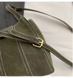 Detail of dark green lychee leather bucket bag with white stitching and gold buckle strap