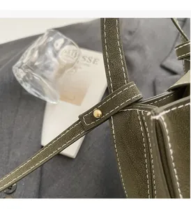 Close-up of olive green bucket bag showing white contrast stitching and gold rivets