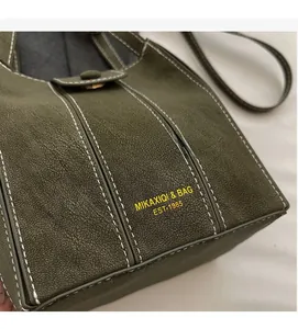 Close-up of dark green bucket bag with white contrast stitching and gold buckle