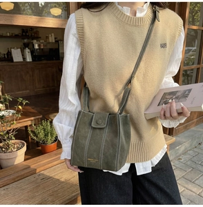 Detail of olive green frosted bucket bag with white contrast stitching and magnetic buckle