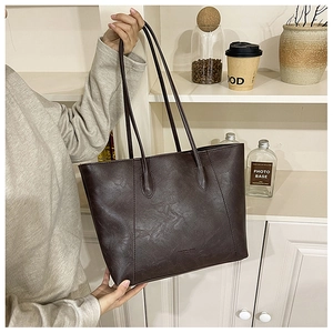 Detailansicht der genarbten Kunstledertextur und des Mode-Logos auf der großen braunen Tote-Bag