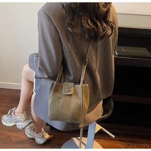 Detail of olive green bucket bag with white contrast stitching and gold brand logo