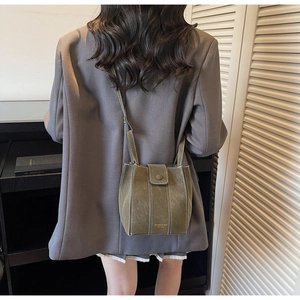 Close-up of olive green suede bucket bag with white contrast stitching on grey blazer