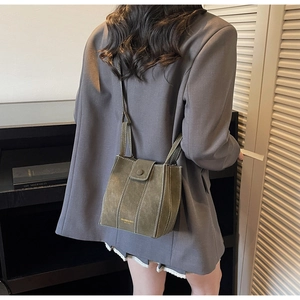 Detail of olive green suede bucket bag with white contrast stitching on model