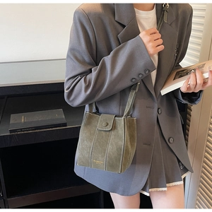 Detail of olive green suede crossbody bag with contrast stitching and gold lettering