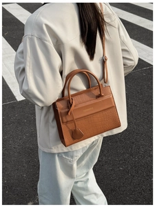 Detail van bruine crossbodytas met krokodillenpatroon gedragen door een model
