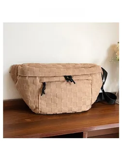 Close-up of khaki woven chest bag with adjustable black nylon strap on wooden surface
