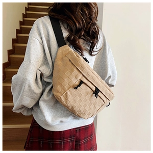 Detail of light brown woven checkered crossbody bag with black nylon strap on model