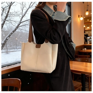 Close-up of cream tote bag with brown straps and fine vertical stitching detail