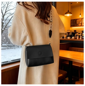 Detail of black matte crossbody bag with a colorful geometric woven strap in a cozy cafe