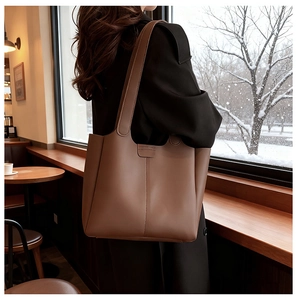 Detail of a large brown leather tote bag worn by a model in a cafe setting