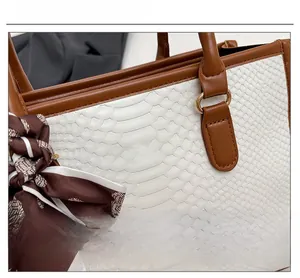Detail of white crocodile pattern tote bag with gold logo and silk scarf on handle