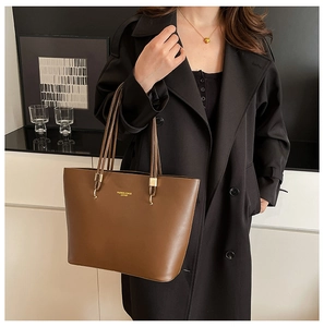 Detail of a brown leather tote bag showing golden brand text and sleek shoulder strap
