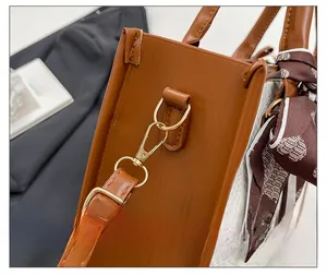 Detailed view of color-block bag with brown leather, metal hooks, and heart scarf handle